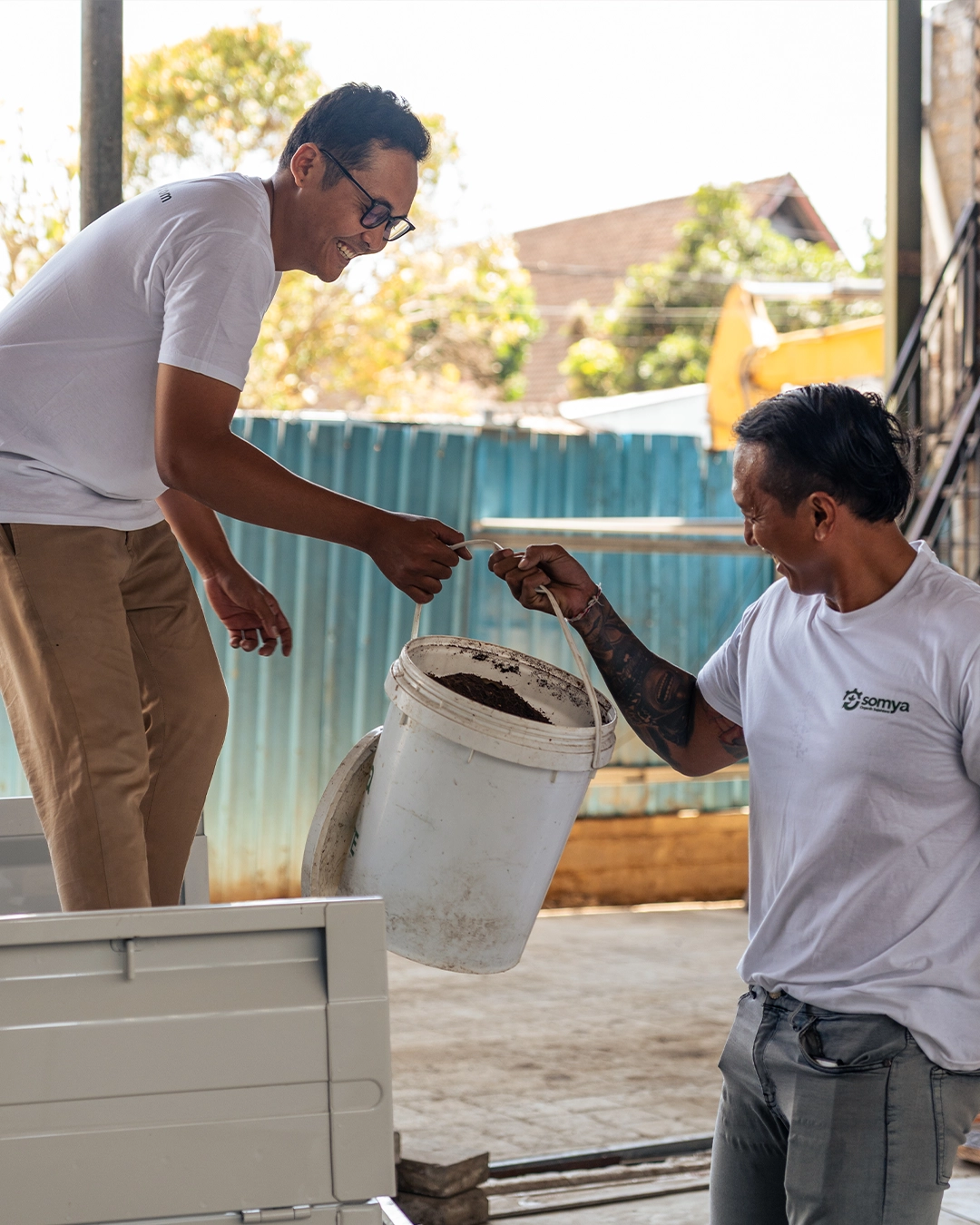 Dua petugas SOMYA mengangkat ember sampah organik dari tempat penampungan ke truk